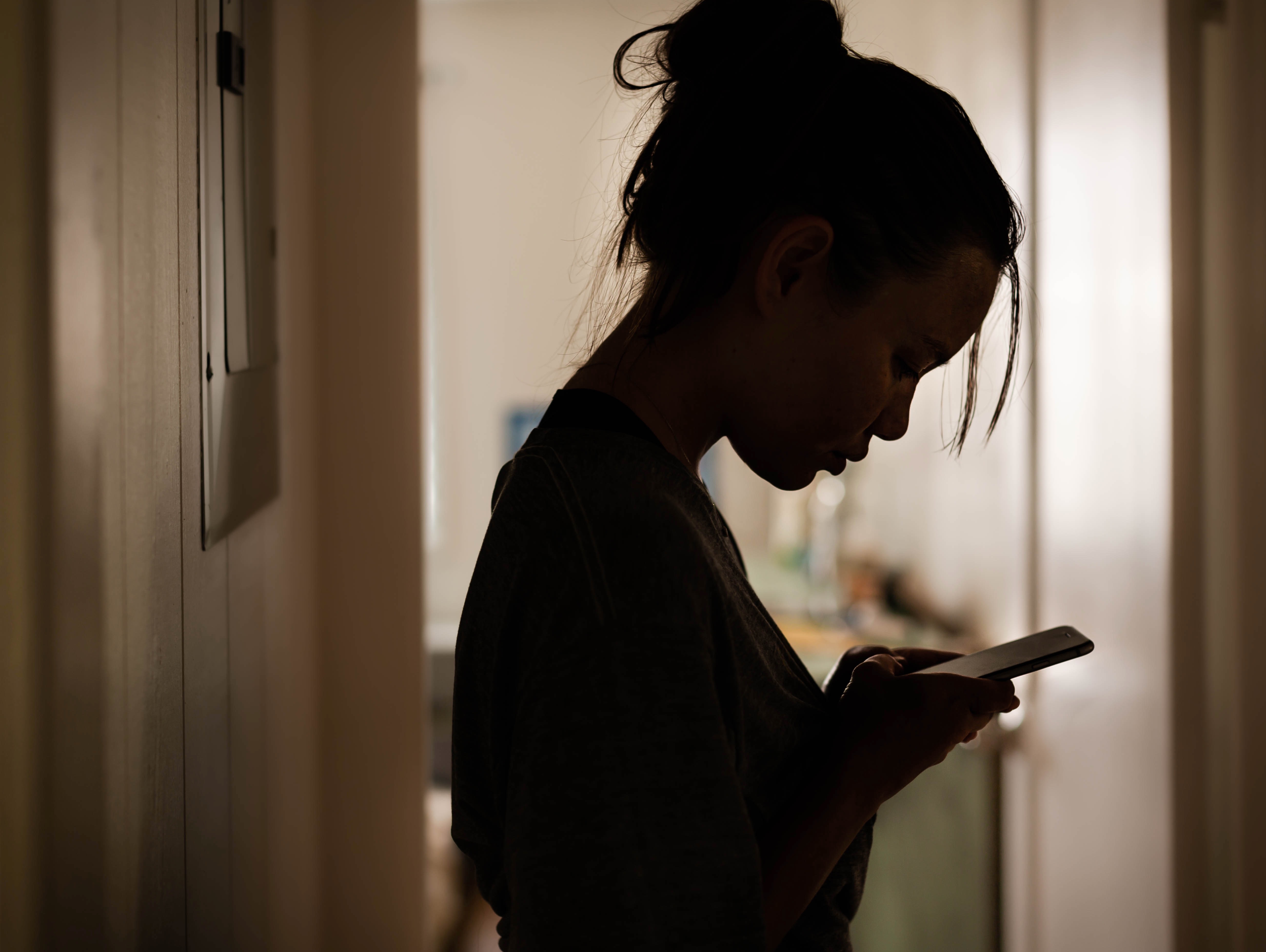 silhouette of a woman standing in a hallway looking at her phone
